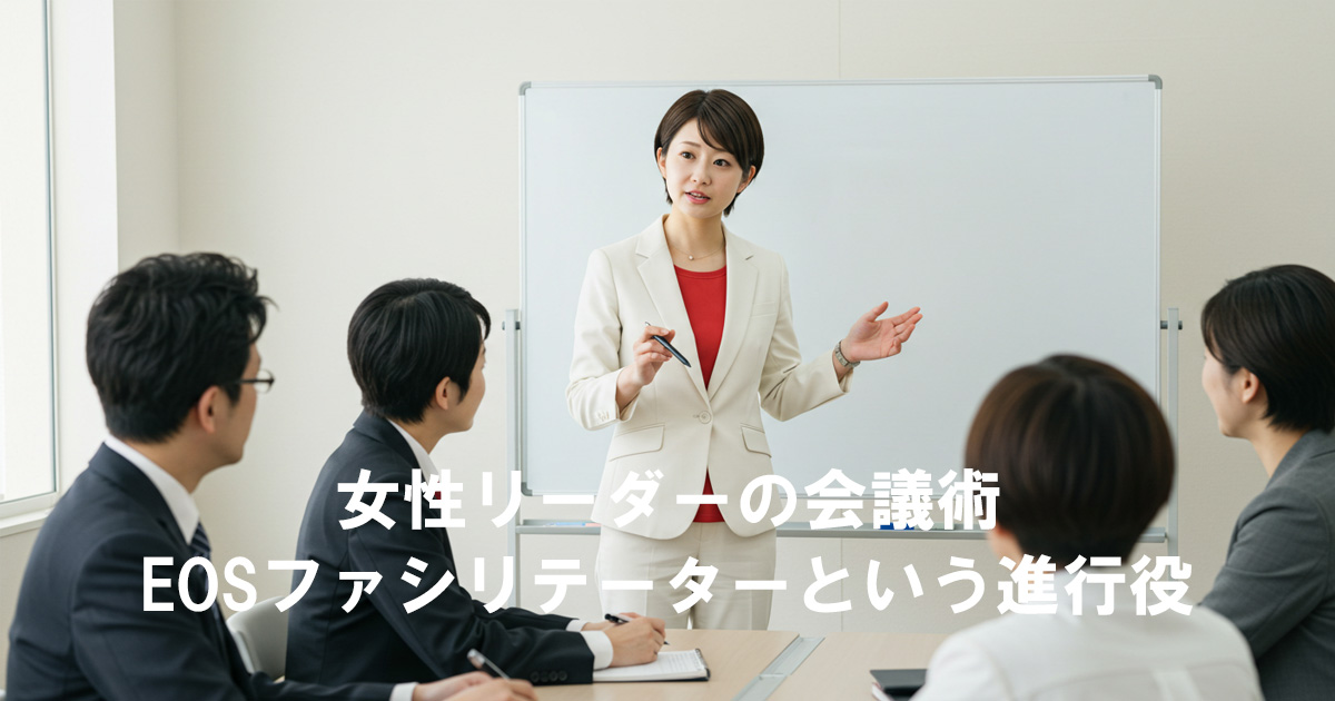 白スーツと赤いインナーを着た女性リーダーがホワイトボード前で会議を進行し、周囲のメンバーに説明している様子